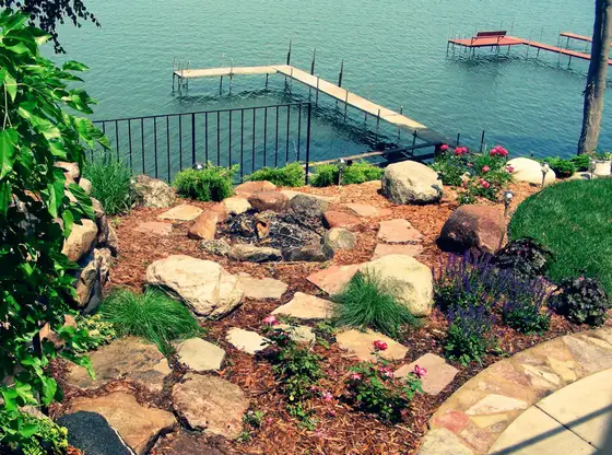 Natural stone fire pit and flagstone patio with boulder edging overlooking a lakeside dock