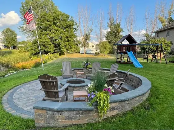 Circular paver patio with a stone seating wall, fire pit and Adirondack chairs in a backyard at golden hour