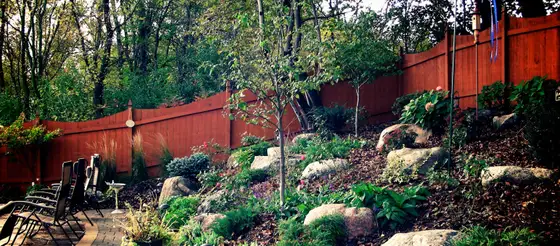 Backyard hillside planting bed with boulder accents and a cedar privacy fence beside a paver patio