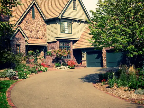 Curved driveway with brick paver edging and colorful flower beds in front of a stone Tudor-style home