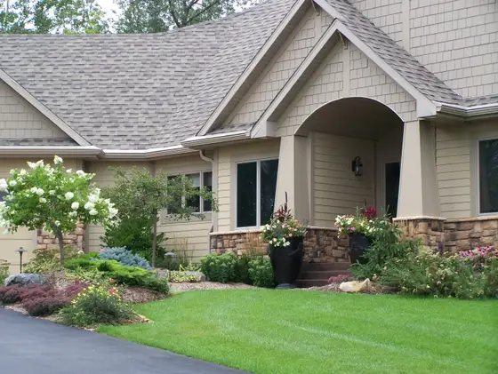 Front entry landscaping in Lakeville with a hydrangea tree, layered evergreens, and flower planters by a stone porch