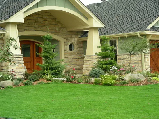 Foundation planting bed with roses, perennials, and a boulder accent framing a stone Craftsman entry in Edina