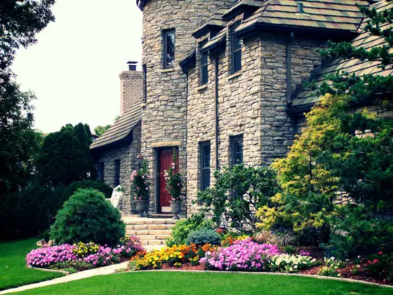 Stone home entrance with stone steps and a vivid border of mixed annual flowers