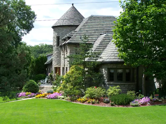 Stone turret home in Golden Valley with a curved border of colorful annual flowers and a manicured lawn