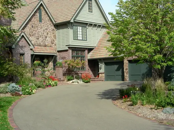Stone-and-brick Tudor home in Eden Prairie with a paver-edged driveway and colorful salvia and grass plantings