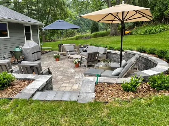 Curved multi-level paver patio with a stone seating wall, steps, and shaded lounge furniture