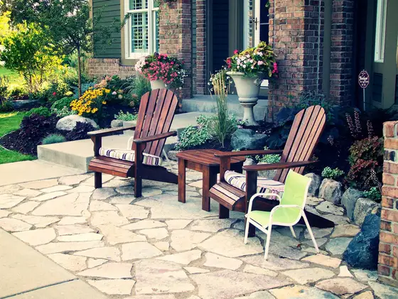 Flagstone front patio with wooden Adirondack chairs and flower planters beside a brick home