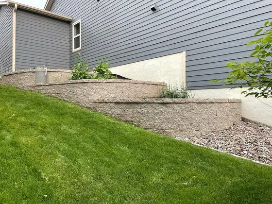Tiered concrete block retaining wall with a planting pocket along the side of a home
