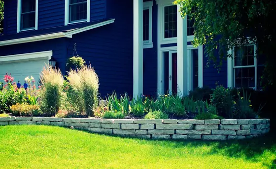Low natural stone retaining wall with ornamental grasses bordering a green lawn