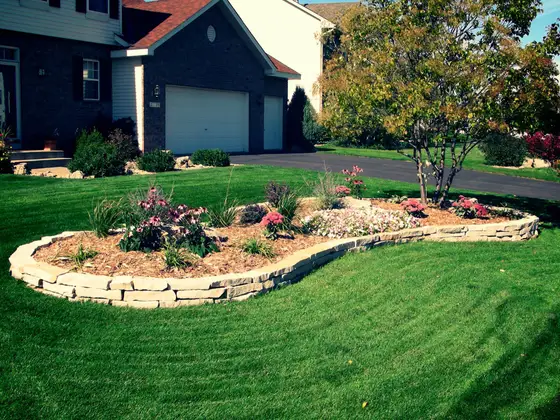 Curved natural stone retaining wall edging a front-yard planting island with daylilies and ornamental grasses