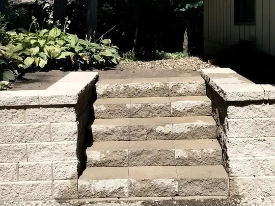 Concrete block retaining wall with built-in steps leading up to a shaded hosta garden