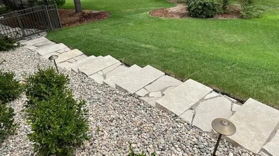 Flagstone step path through a river-rock bed with path lights beside a manicured lawn