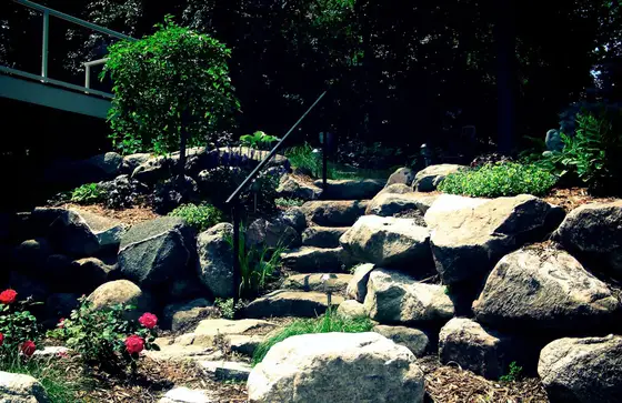 Natural boulder steps with a metal handrail climbing a landscaped hillside garden